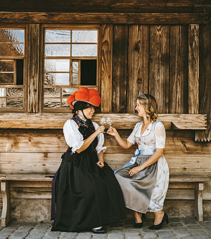 Vor einem der Häuser des Volgtsbauernhofs prosten sich zwei Frauen in Tracht zu. Foto: Weinparadies Ortenau e.V.