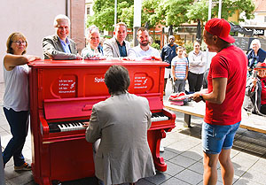 Öffentliches Klavier mit Klavierspieler und sich präsentierenden Honoratior*innen